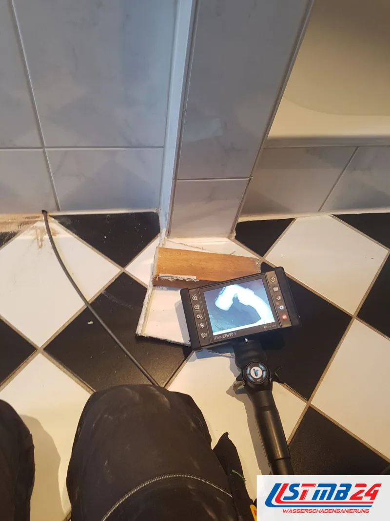 Endoskop mit Monitor auf Schachbrettfliesen, die Sonde führt in eine Öffnung am Sockel neben der Wanne