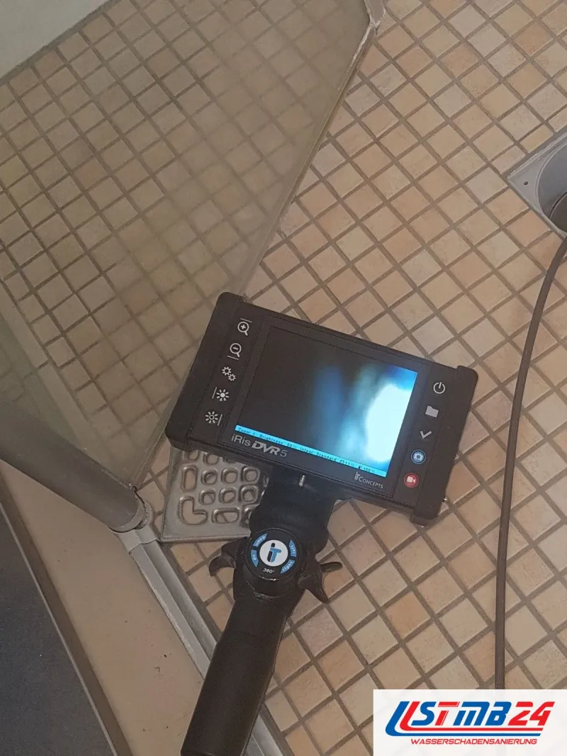 Endoskop mit Monitor über einem Mosaikboden, die Sonde führt zum Ablauf einer Dusche