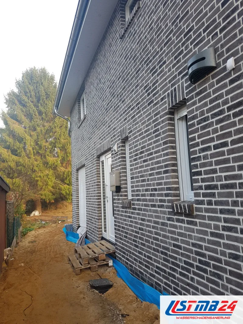 Klinkerhaus mit aufgegrabenem Graben entlang der Außenwand, blaue Folie am Sockel und Paletten, die Kellerwand liegt frei
