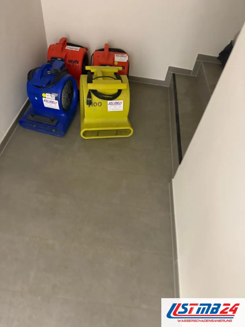 Vier Ventilatoren in Blau, Gelb und Rot mit STMB24-Aufklebern stehen in der Ecke eines gefliesten Treppenflurs bereit