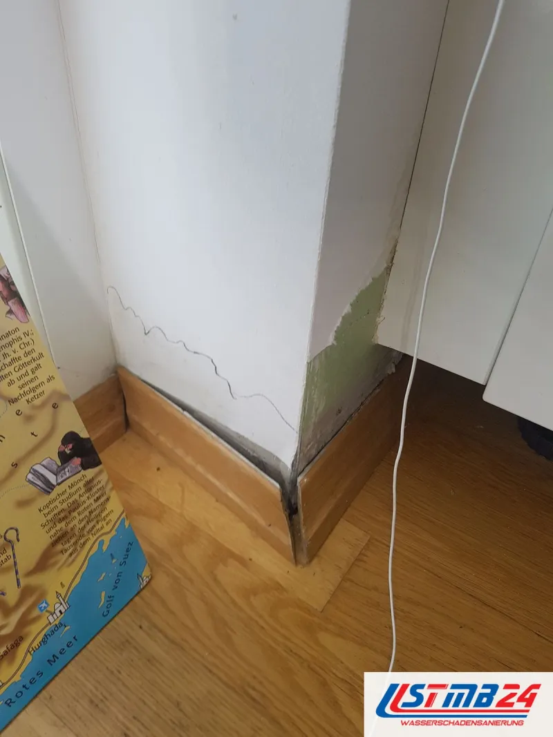 Ecke eines Pfeilers über Eichenparkett, am Fuß ist der Anstrich grünlich verfärbt und abgeplatzt, die Sockelleiste dunkel