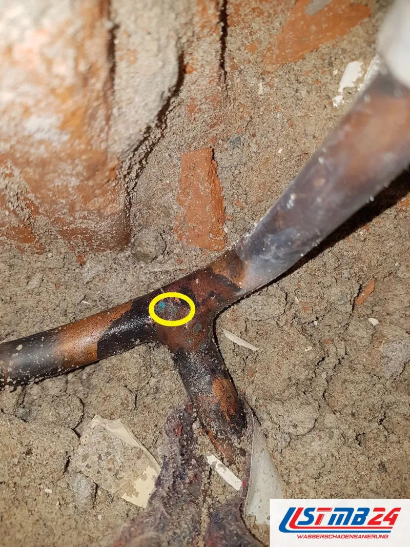 Kupferrohr mit T-Stück in Sand und Ziegelbruch, gelb umkreist ein winziges Korrosionsloch an der Abzweigung