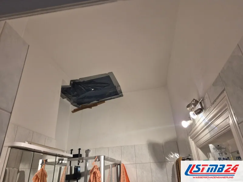 Baddecke mit einer Öffnung, die mit schwarzer Folie und Klebeband abgedeckt und mit einer Latte gestützt ist, darunter die Dusche
