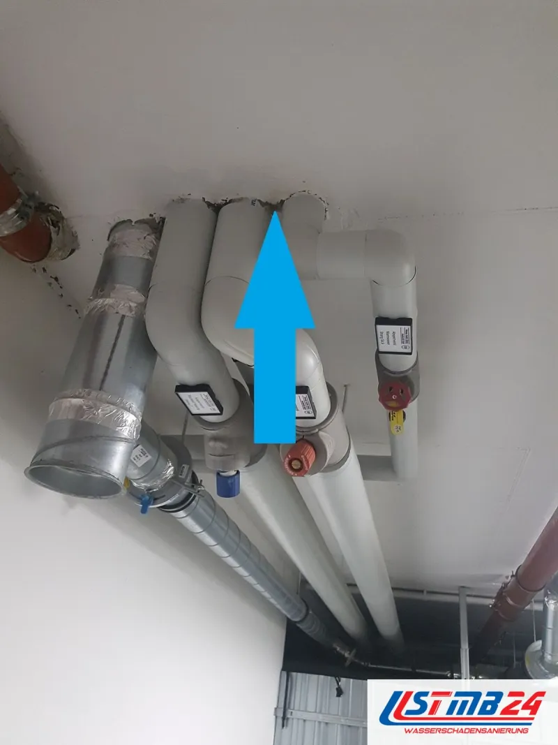 Rohrstrang unter der Decke mit Wasserleitungen und Abflussrohr, ein blauer Pfeil zeigt auf die nasse Durchführung