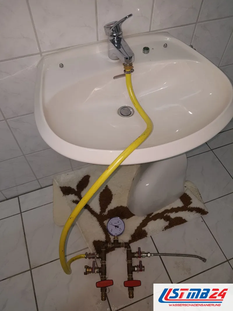 Waschbecken mit gelbem Schlauch zu einem Prüfgerät mit Manometer auf dem Fliesenboden