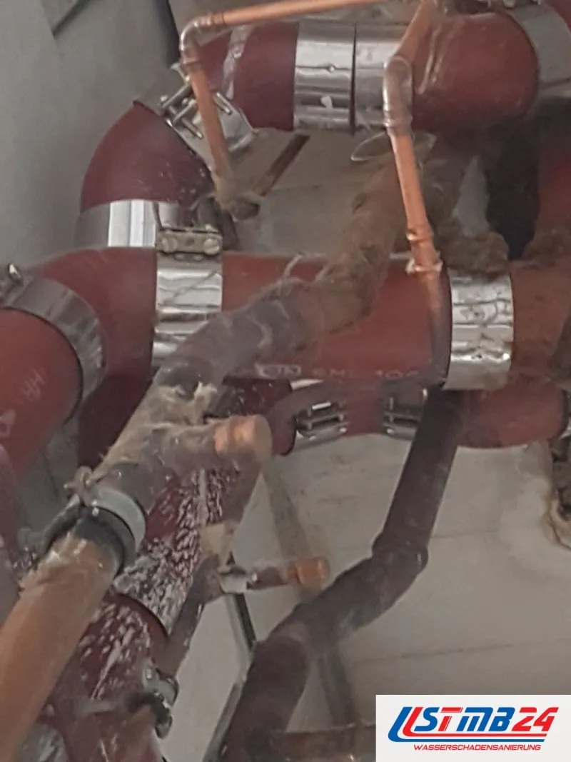 Rot gedämmte Heizungsrohre und Kupferleitungen mit silbernem Klebeband in einer geöffneten Decke