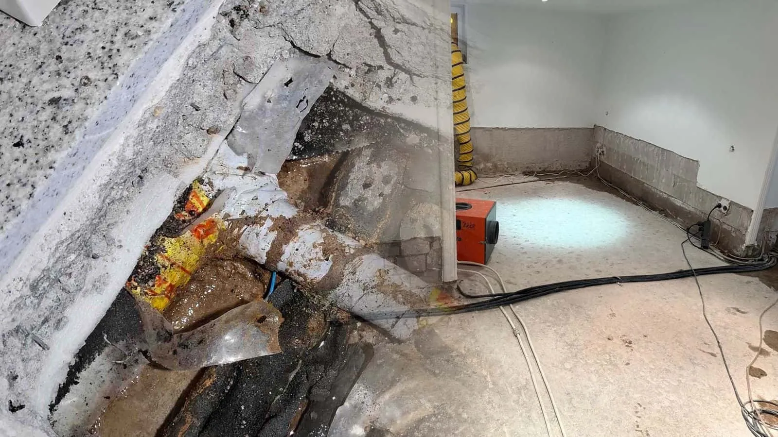 Souterrain mit abgeschlagenem Sockelputz, ein orangefarbenes Gerät auf dem Estrich, Kabel am Boden