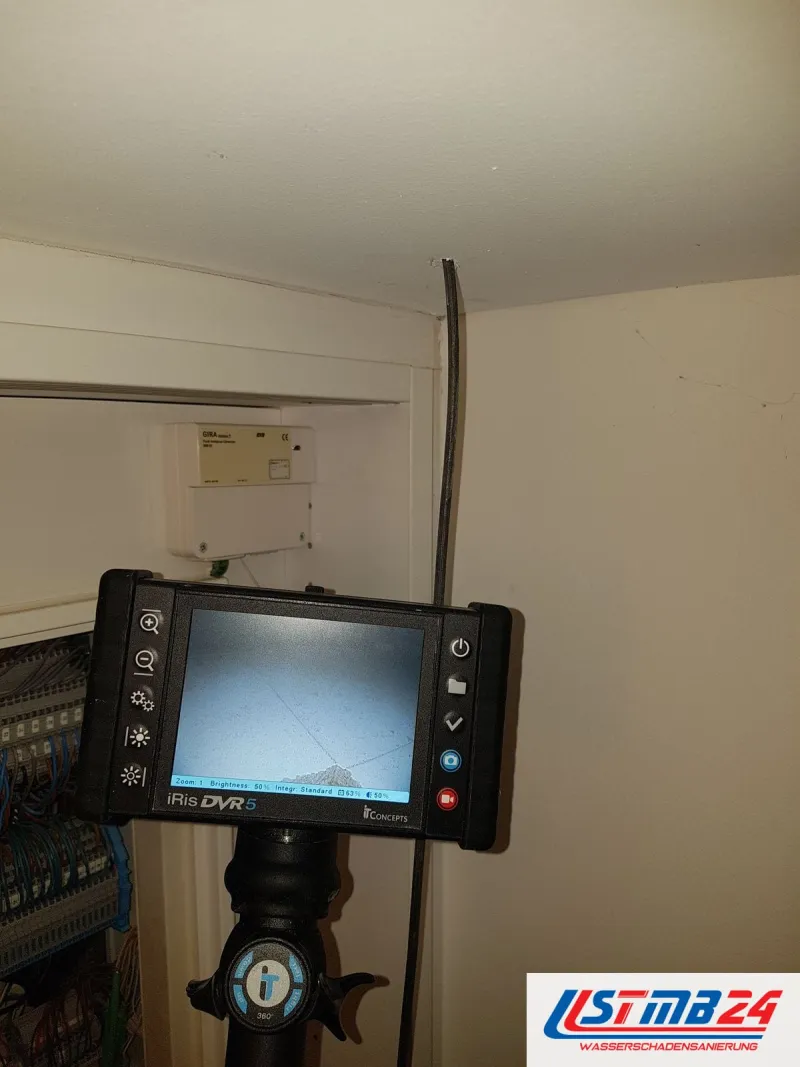 Endoskop mit Monitor, die Sonde führt durch ein kleines Bohrloch in die Decke über einem offenen Elektroverteiler