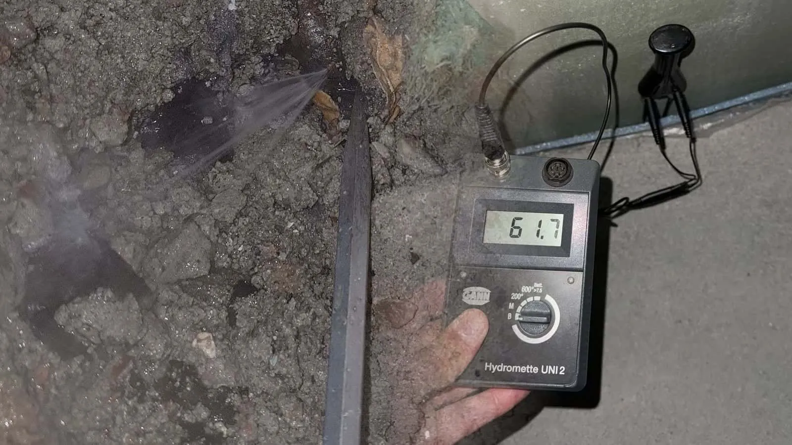 Messgerät mit der Anzeige 61,7, die Elektroden stecken in einer grünen Gipsplatte über dem Estrich