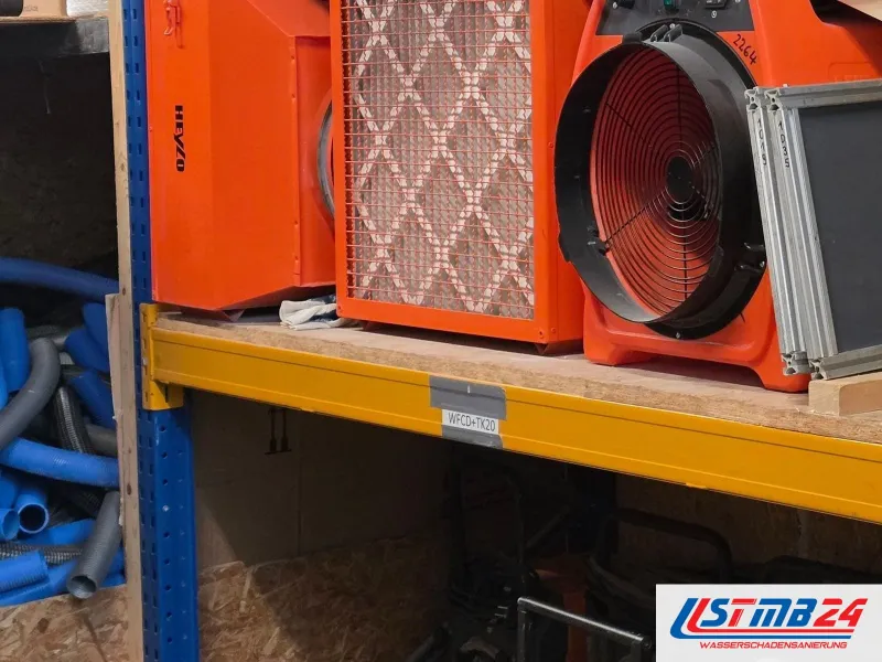 Orangefarbene Geräte im Lagerregal, darunter ein Ventilator mit Schutzgitter, daneben blaue Schläuche