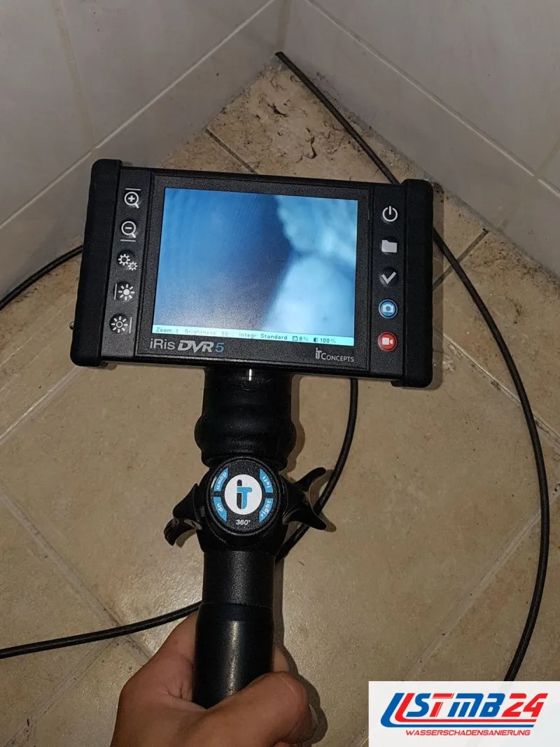 Videoendoskop mit leuchtendem Monitor in der Hand, das Kabel führt zu einer gefliesten Ecke am Boden