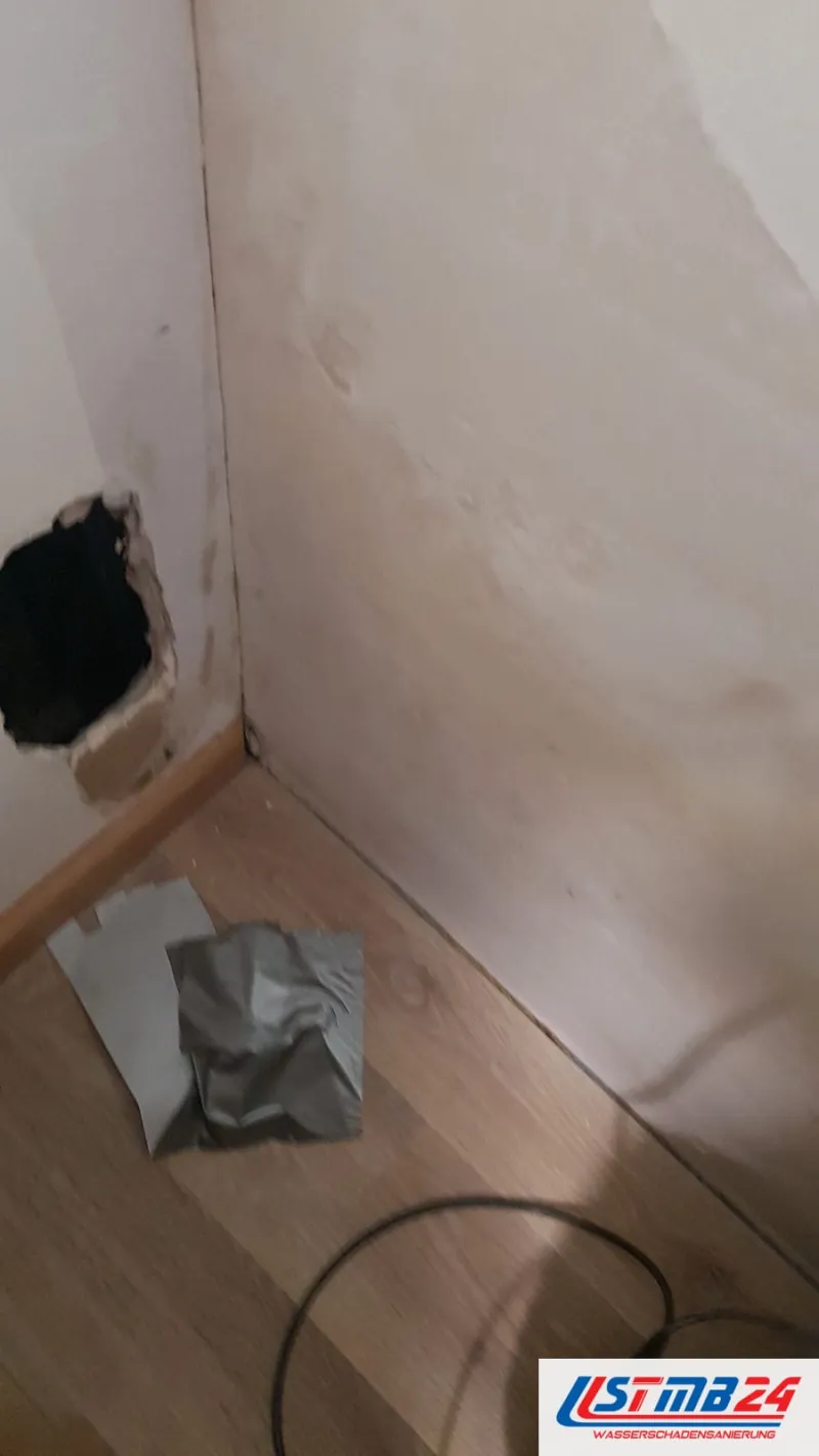 Raumecke mit einer Öffnung unten in der Wand, davor liegt graue Folie auf dem Boden, ein Kabel führt durch den Raum