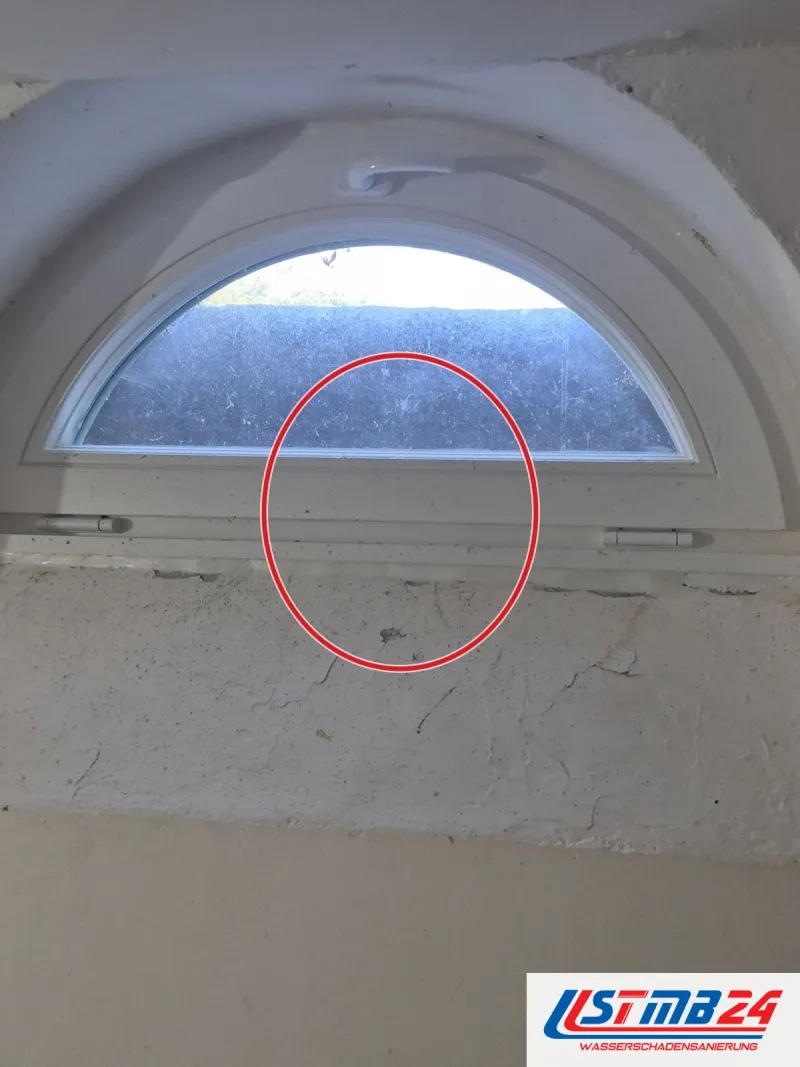 Halbrundfenster mit Kippflügel in tiefer Laibung, darunter abgeplatzte Farbe auf dem Putz, ein roter Kreis markiert die Stelle