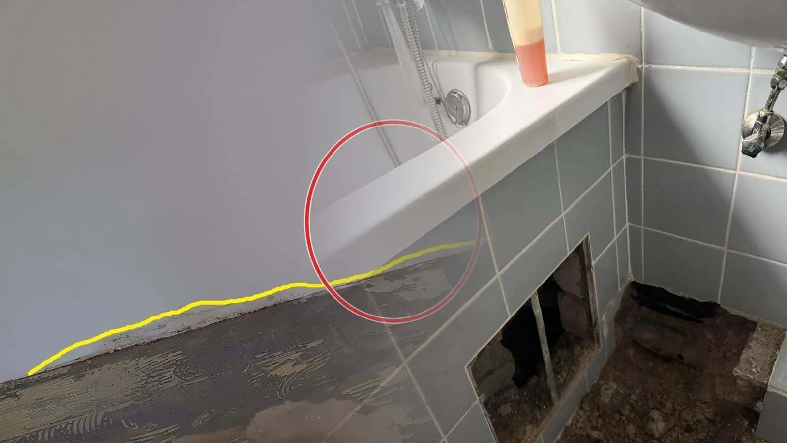 Wanne mit blau gefliester Schürze, zwei Fliesenfelder herausgenommen, dahinter feuchter Untergrund mit dunklen Stellen
