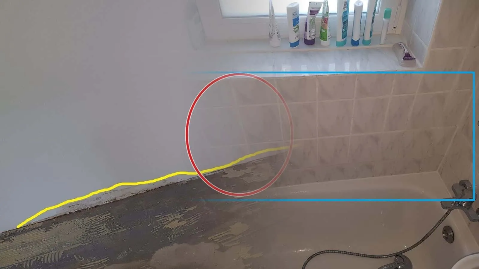 Wanne unter einem Fenster, ein blauer Rahmen umfasst die marmorierten Wandfliesen über dem Wannenrand