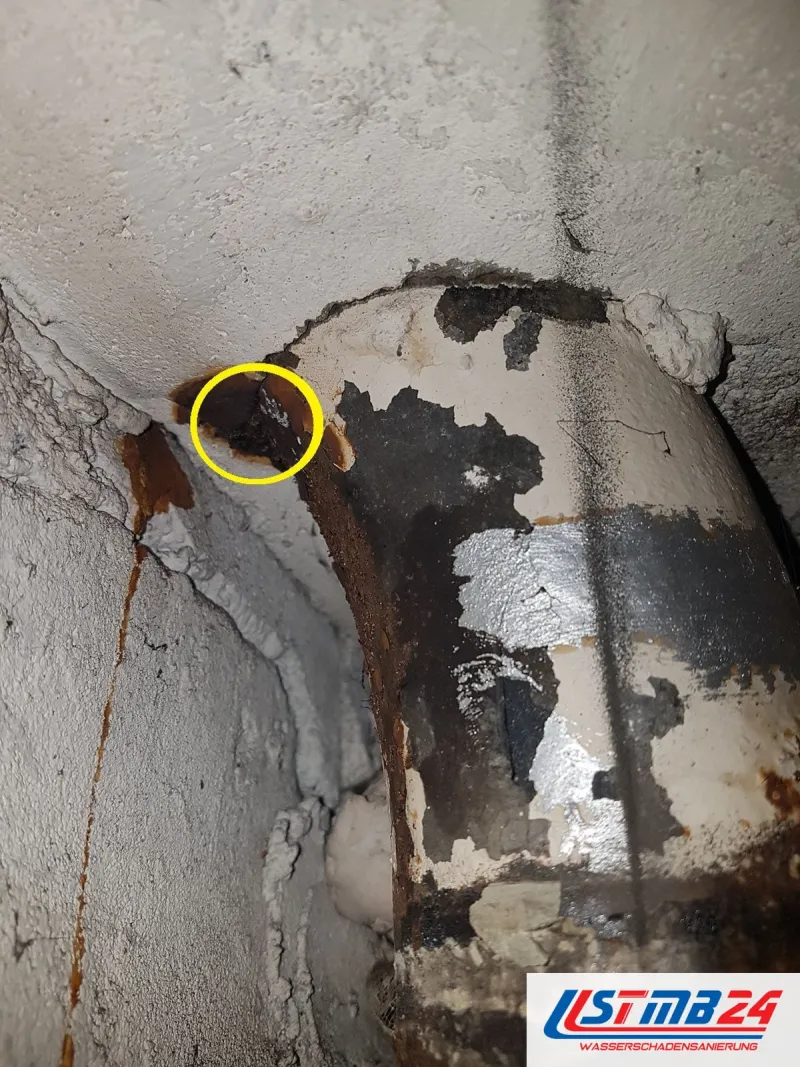 Altes Gussrohr unter der Decke, gelb eingekreist ein Loch im Rohr, darunter Roststreifen an der Wand