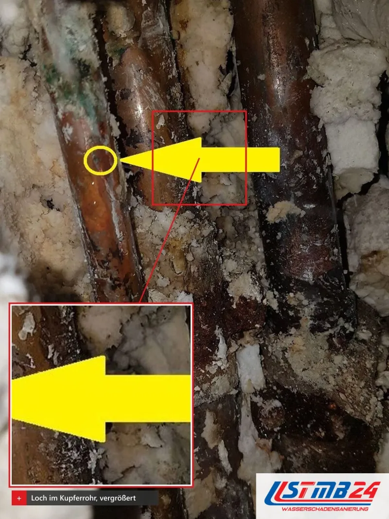 Kupfer- und Stahlrohre in einem offenen Schacht mit Schaum und Rost, vergrößert ein gelb umkreistes winziges Loch im Kupfer