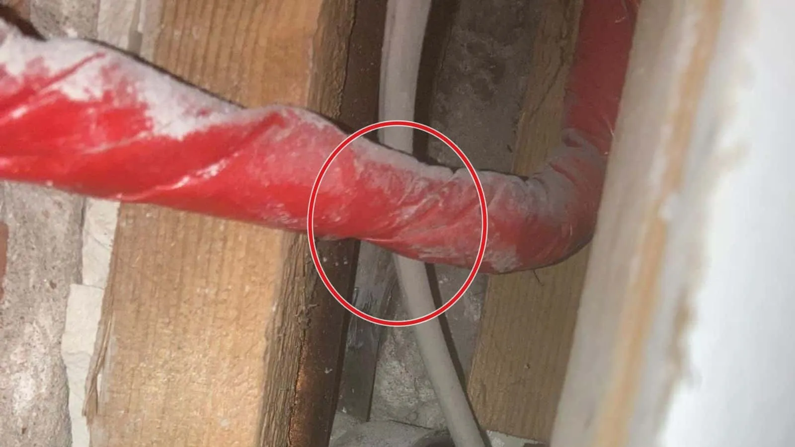 Geöffnete Wand mit Holzbalken und rotem Rohr, ein roter Kreis markiert die Stelle