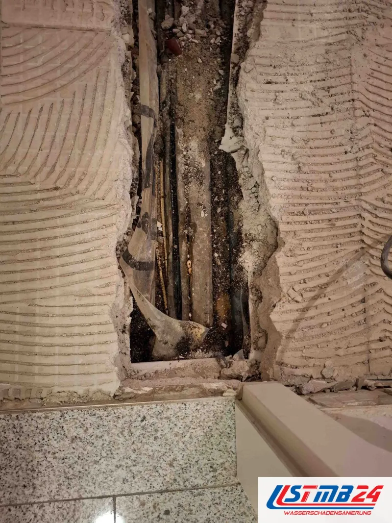 Aufgestemmter Leitungsschlitz im Boden mit Rohren und Dämmung, ringsum Kammspuren von Fliesenkleber, unten Granitfliesen