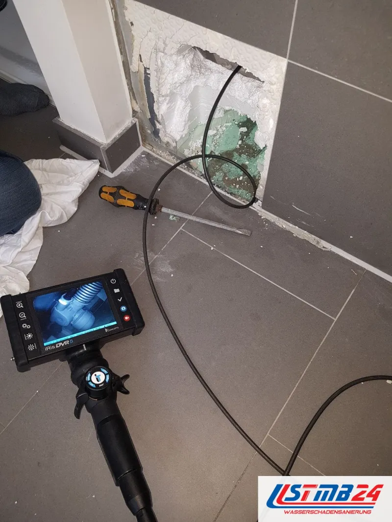 Videoendoskop mit Monitor vor einem geöffneten Fliesensockel, das Kabel führt in die Öffnung, ein Schraubendreher daneben