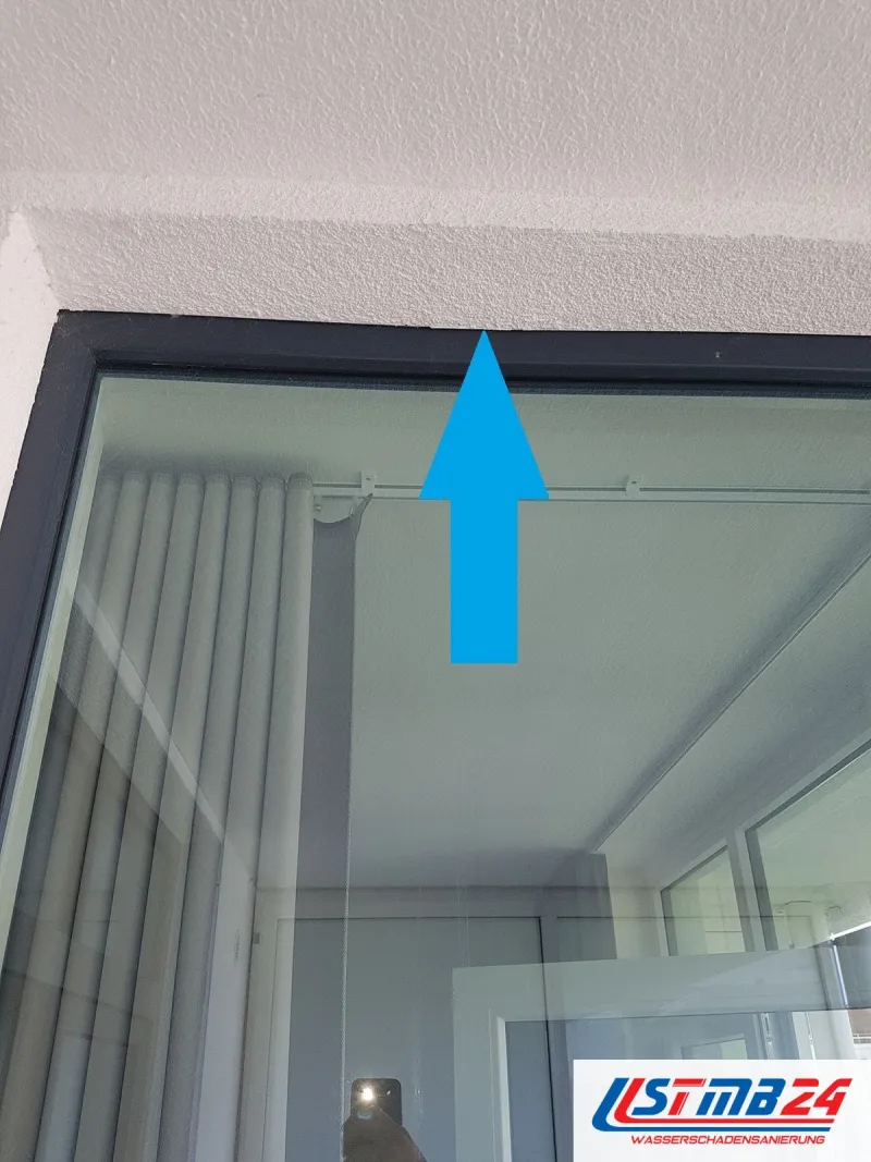 Fenster mit dunklem Rahmen von innen, ein blauer Pfeil zeigt auf den oberen Anschluss zwischen Rahmen und Laibung