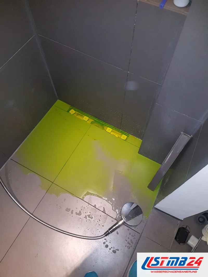 Duschboden mit leuchtend grüner Färbeflüssigkeit, die Brause liegt auf den grauen Fliesen, das Wasser läuft zur Rinne
