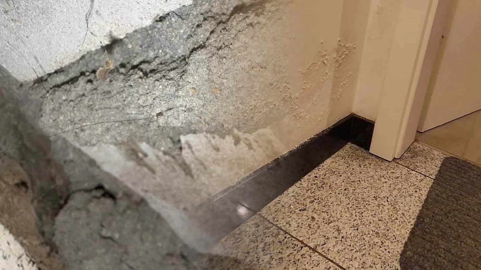 Fleckiger Wandfuß an einer Tür, dahinter Schläuche