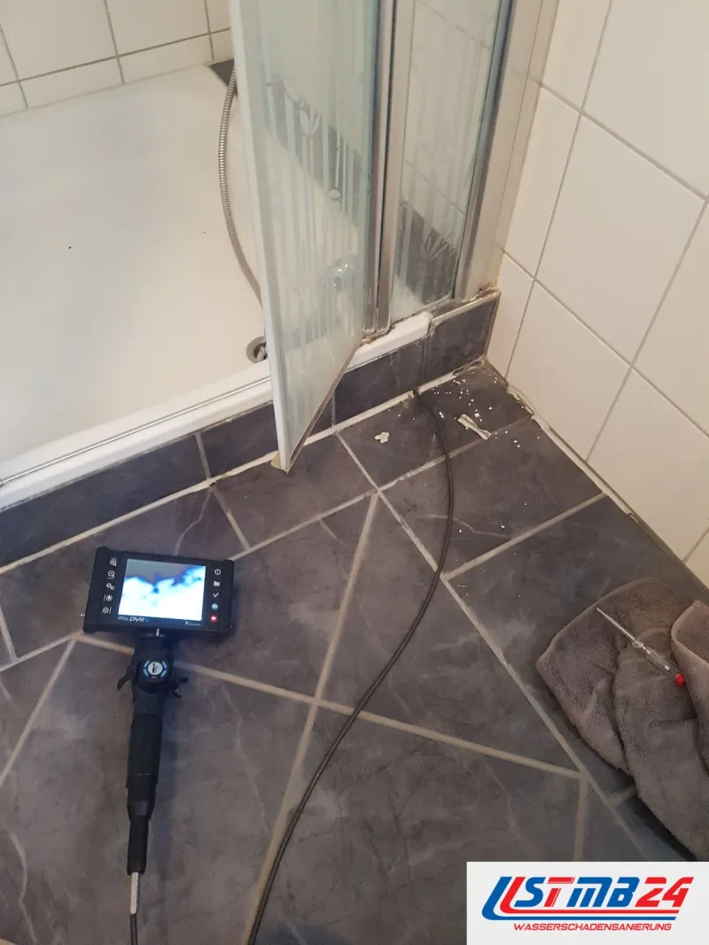 Endoskop mit Monitor auf dunklen Fliesen vor der Glasabtrennung einer Dusche