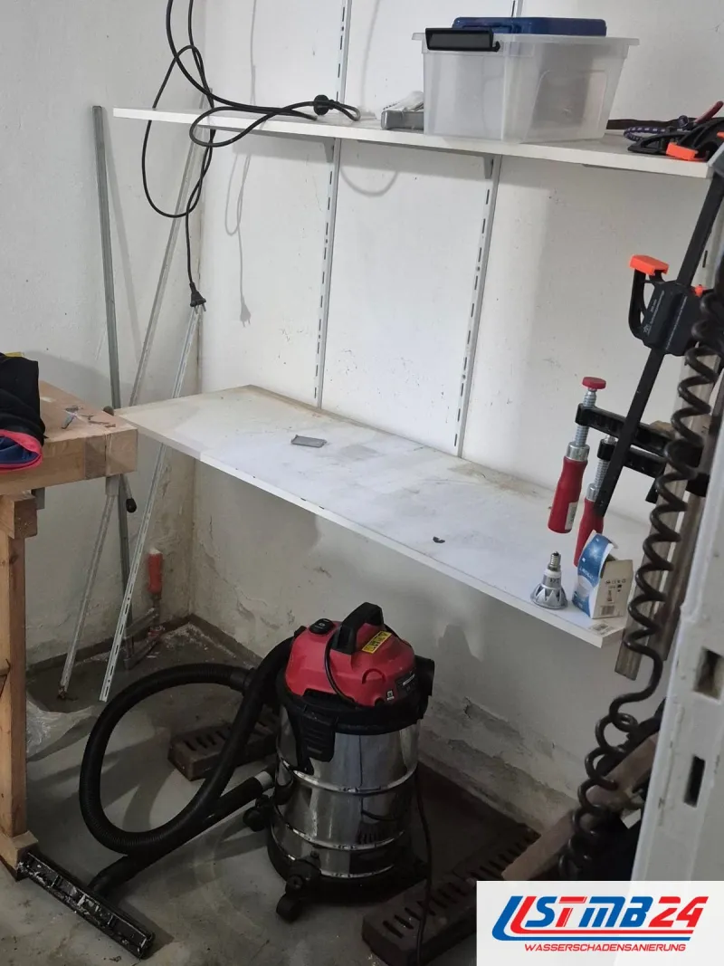 Hobbykeller mit Werkbank und Wandregal, davor ein Nasssauger mit Schlauch auf dem fleckigen Boden