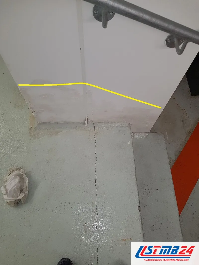 Treppenabsatz mit einem langen Riss im grauen Estrich, an der Wand darüber zeigt eine gelbe Linie die Feuchtegrenze