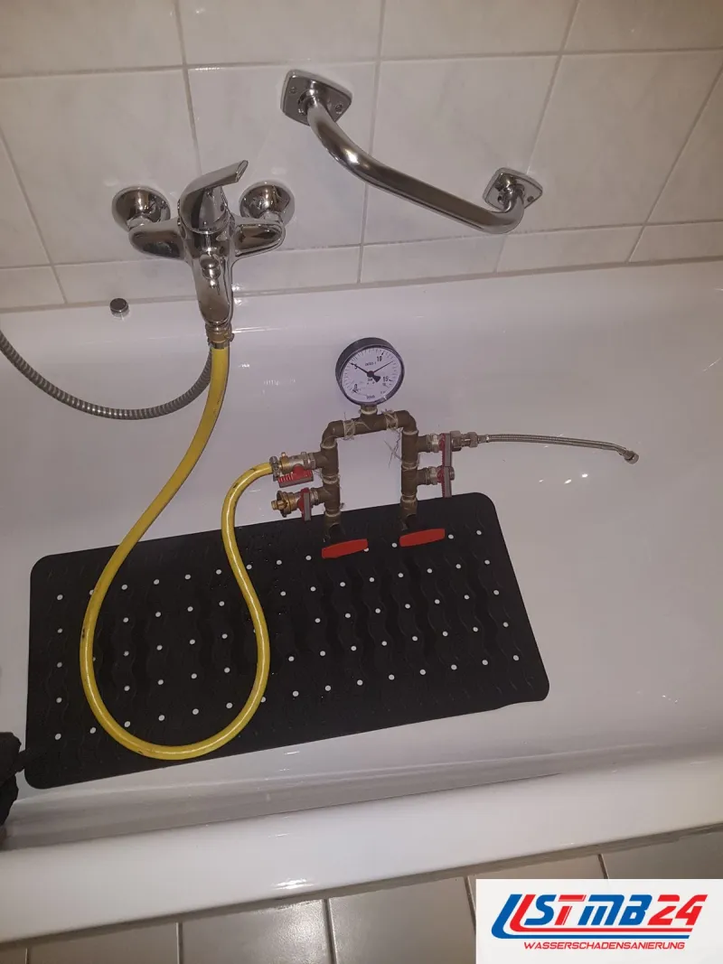 Druckprüfgerät mit Manometer und gelbem Schlauch an der Wannenarmatur, abgelegt auf der Matte in der Badewanne