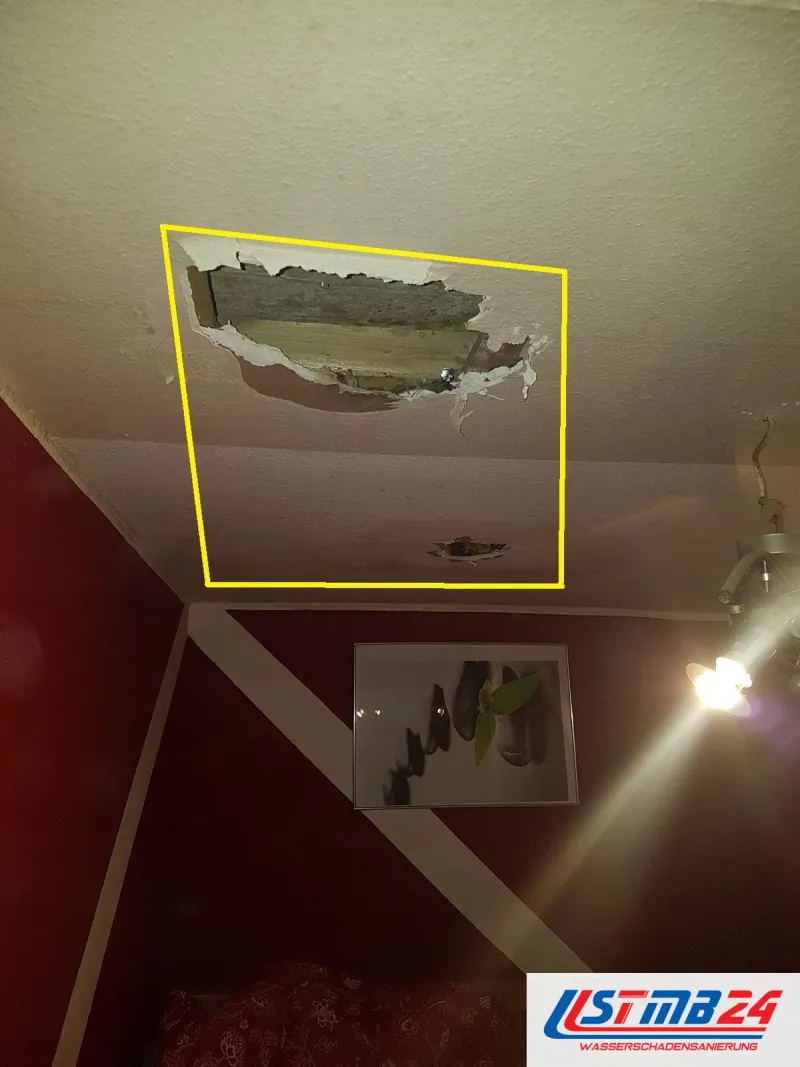 Aufgebrochene Decke über einem Raum mit roter Wand, die Öffnung gelb umrandet, darunter ein kleineres Loch im Putz