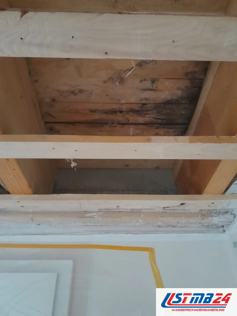 Holzschalung an einer Decke mit dunklen Wasserflecken über einem Türsturz, unten gelbes Klebeband