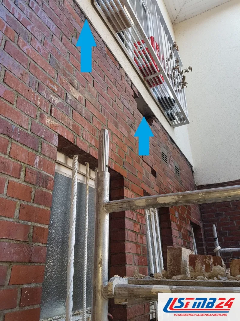 Klinkerfassade mit Gerüst, zwei blaue Pfeile zeigen nach oben auf die Unterseite eines Balkons