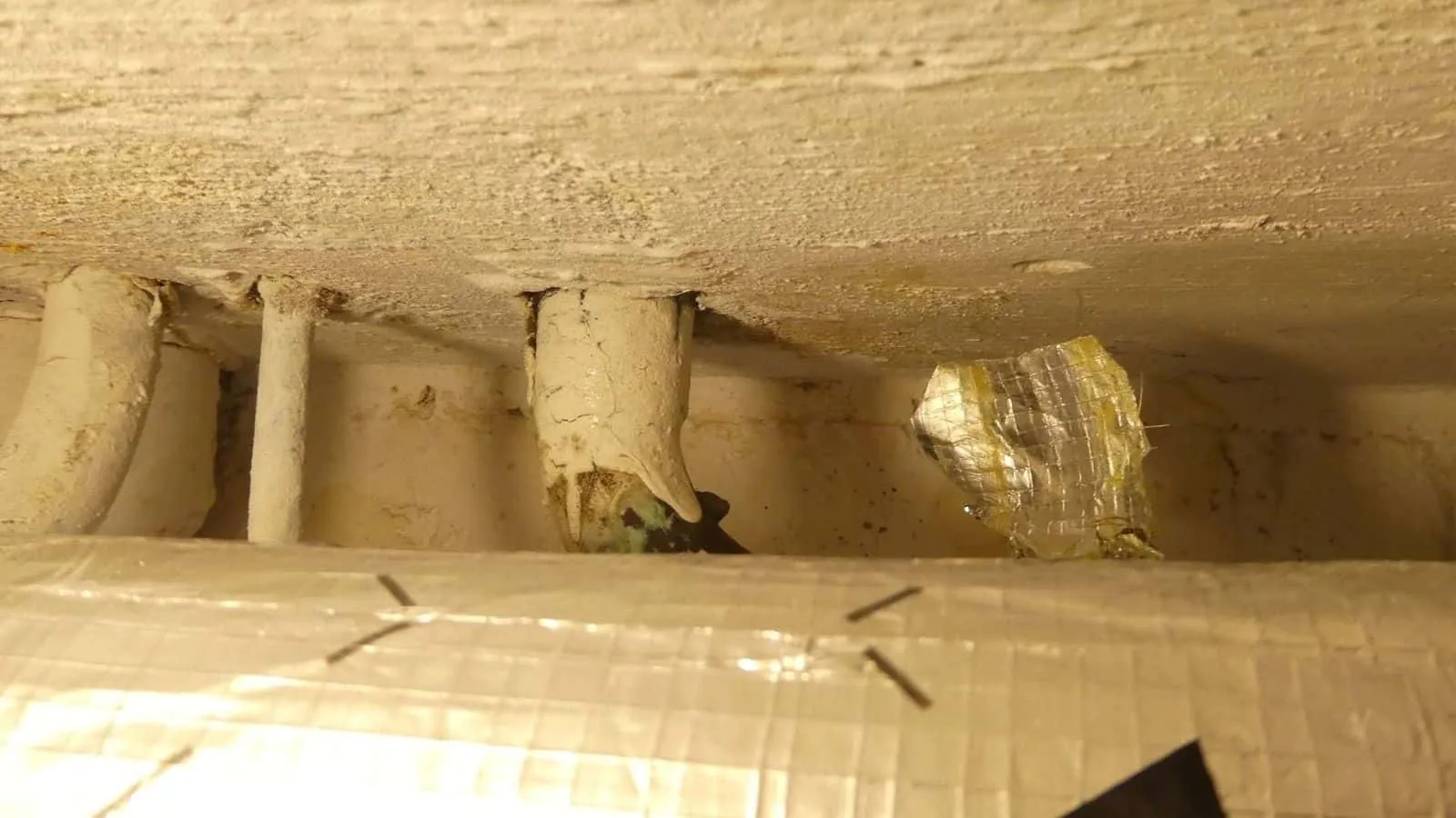 Kellerdecke mit gedämmten Rohren, eine Dämmung mit Alufolie geflickt