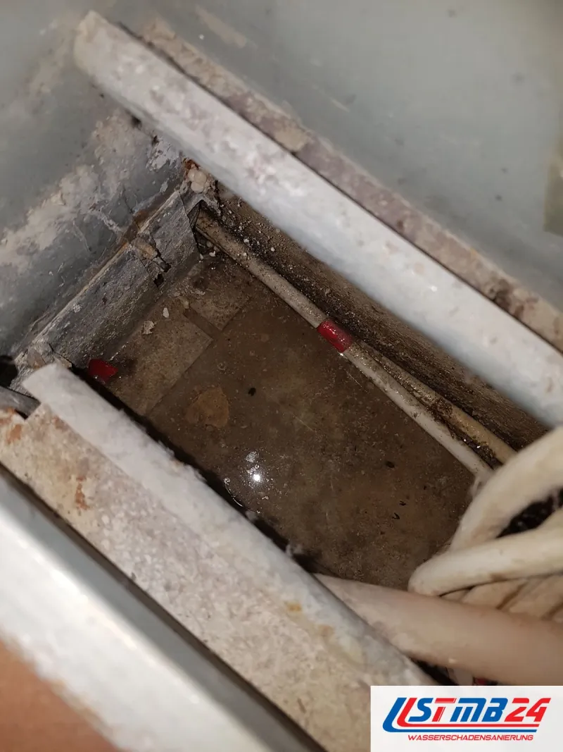 Geöffneter Boden, im Hohlraum steht Wasser zwischen Rohren und Rohrdämmung