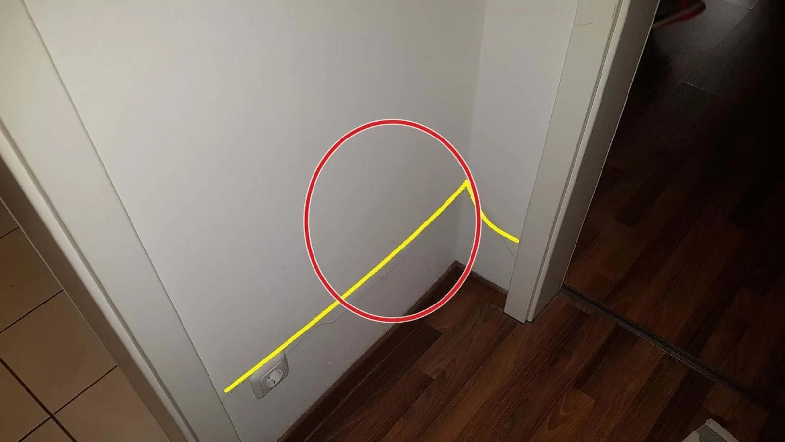 Wandecke neben einer Tür, eine gelbe Feuchtelinie über dunklem Laminat