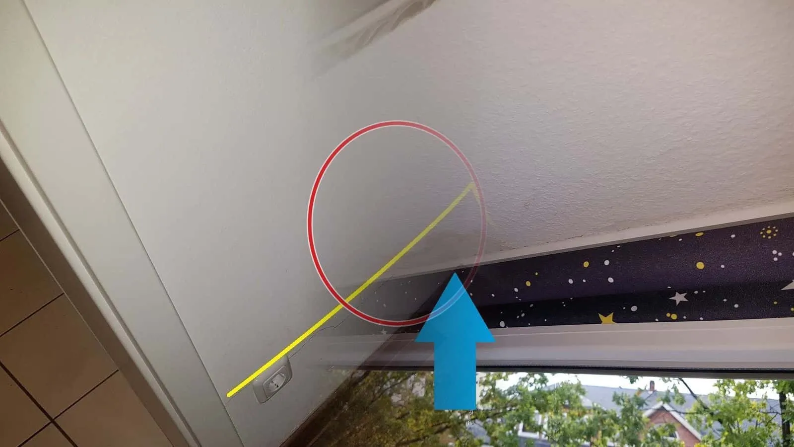 Wasserfleck an der Decke über einem Fenster, ein blauer Pfeil zeigt auf die Stelle über dem Sternenrollo