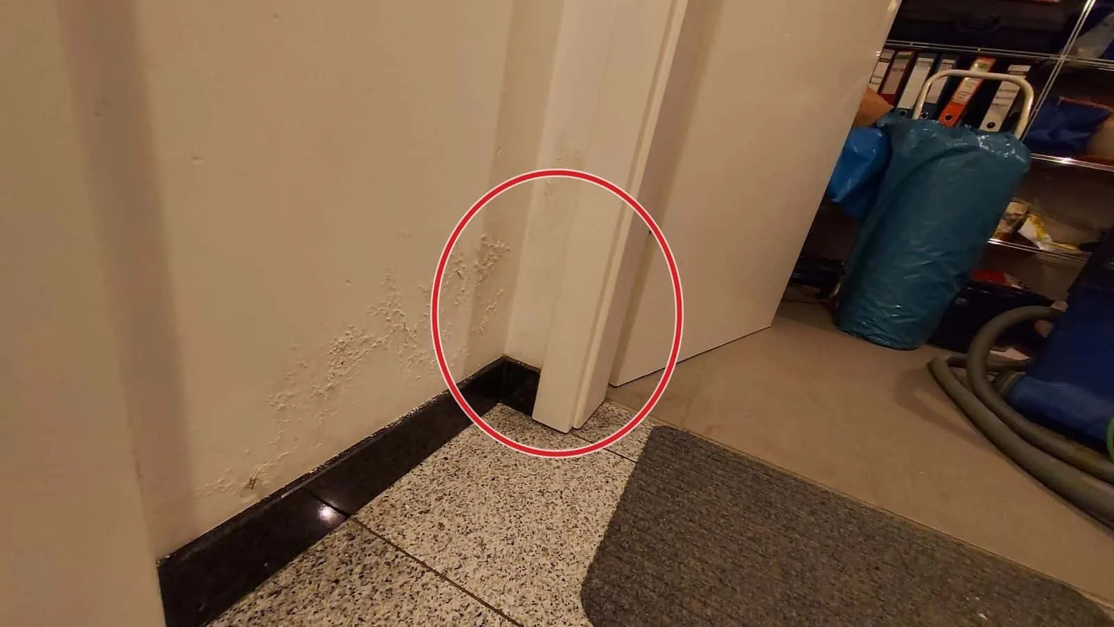 Wandfuß mit dunklen Flecken neben einer Tür, dahinter Trocknungsschläuche am Boden