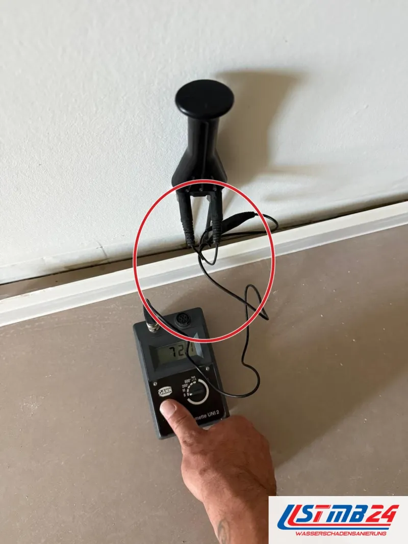 Messgerät mit zwei Elektroden an der Wand über der Sockelleiste, darunter blanker Estrich, ein roter Kreis markiert die Stelle