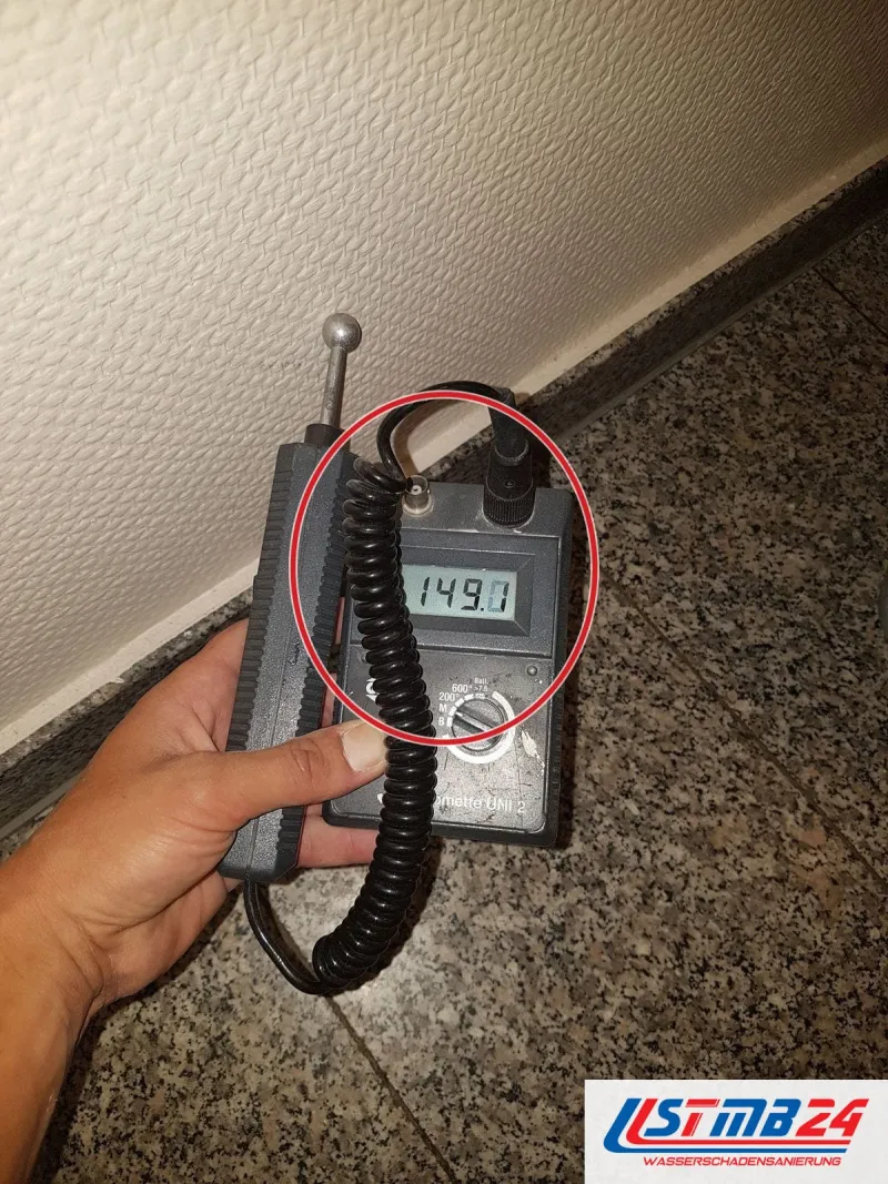 Feuchtemessgerät zeigt 149,1 an einer Raufaserwand direkt über dem Sockel aus poliertem Granit, ein roter Kreis markiert die Stelle