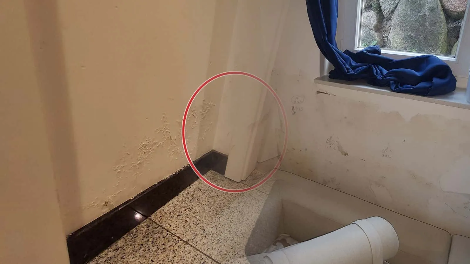 Kellerfenster mit Lichtschacht, darunter Wasserränder und abblätternde Farbe, auf der Fensterbank ein kleiner Granulatentfeuchter