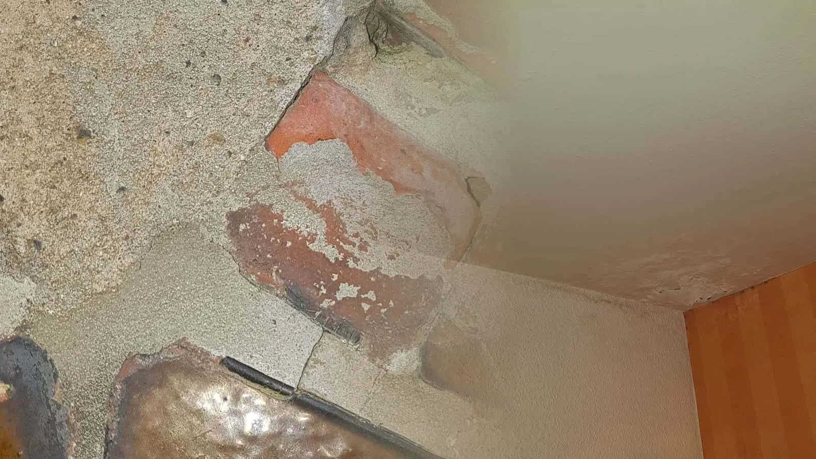 Deckenecke mit Wasserflecken über orange gestreifter Tapete