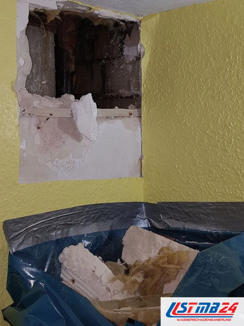 Öffnung unter der Decke einer gelb gestrichenen Wand, am Boden Schutt in blauer Folie