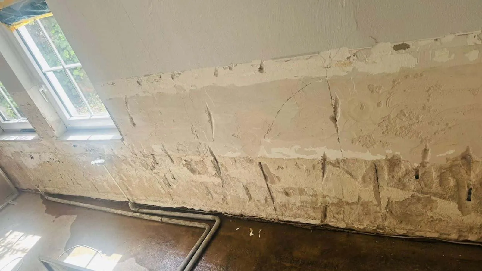 Kellerraum mit Fenster zum Garten: Putz bis zur halben Wandhöhe abgeschlagen, am Boden steht noch Wasser