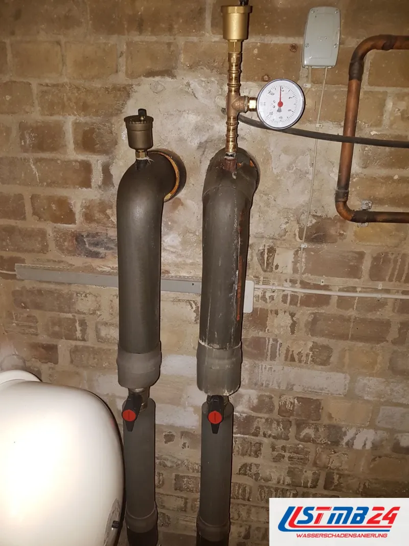 Kellerwand aus Backstein mit gedämmten Rohren, roten Absperrhähnen und einem Manometer an der Leitung