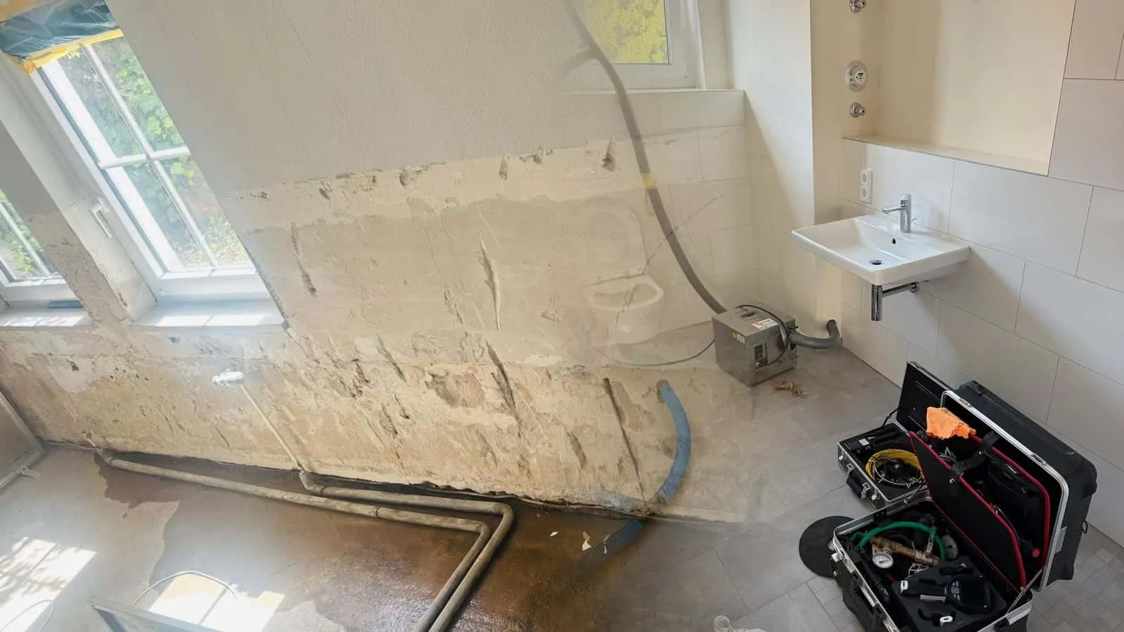 Bad mit blauen Trocknungsschläuchen und Verdichter neben dem WC