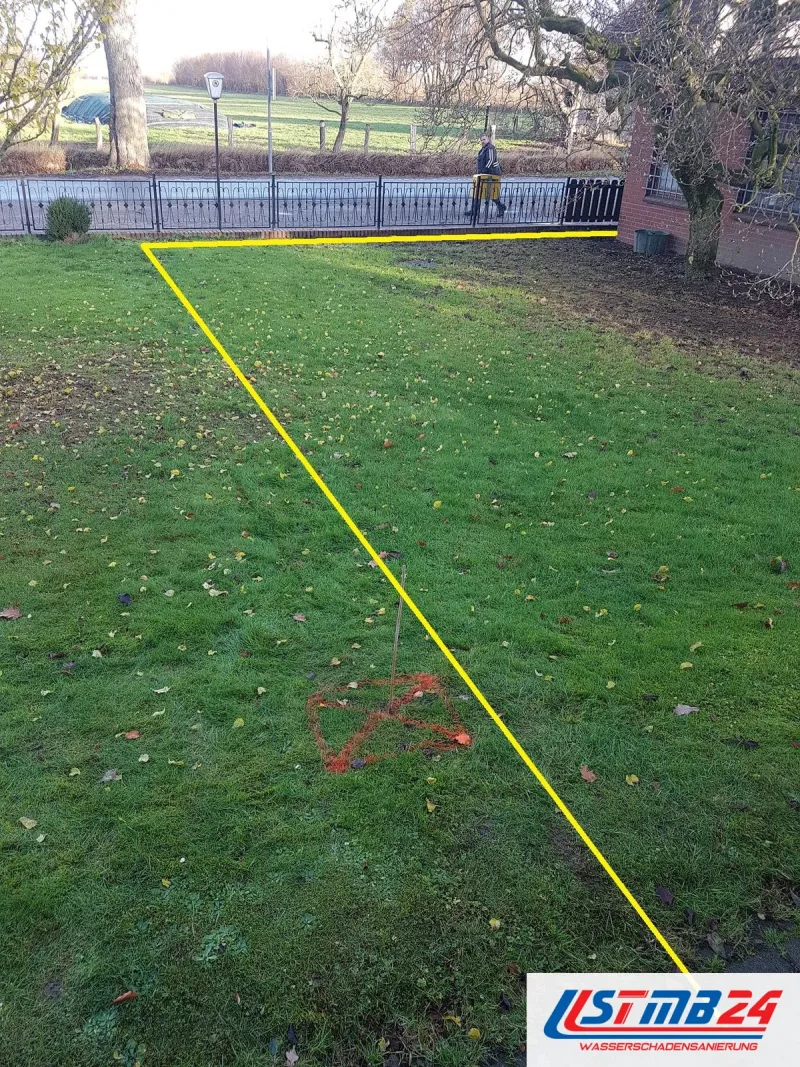 Rasen vor einem Klinkerhaus, eine gelbe Linie zeichnet den Verlauf der Erdleitung nach, die Leckstelle rot auf dem Gras markiert