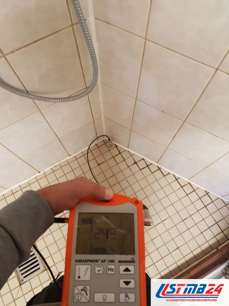 Elektroakustisches Horchgerät in der Hand, das Mikrofon steht in der Ecke einer Dusche mit Mosaikboden