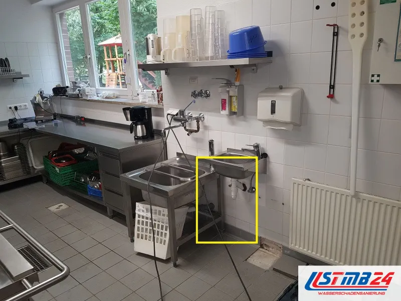Gewerbeküche mit Edelstahlspülen und Arbeitstischen, das Handwaschbecken mit dem Siphon darunter gelb markiert